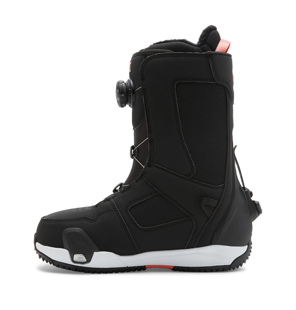 A left-side view of the DC Shoes Women’s Phase BOA® Pro Step On® Snowboard Boot features a black design with a thick white sole, black laces, and a Dual Zone BOA® Fit System dial on the side. Red accents appear near the top and heel.