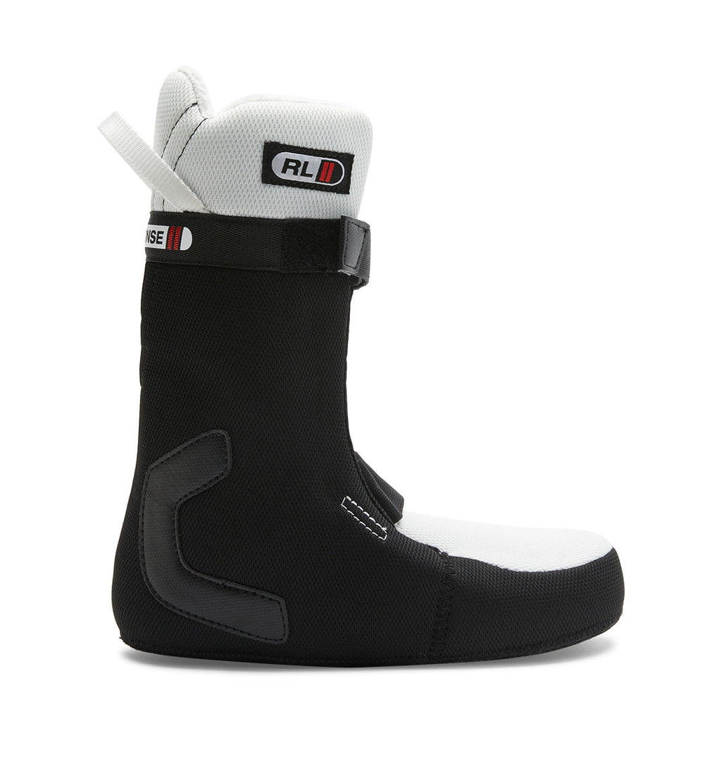 A side view of the DC Shoes Women’s Lotus BOA® Snowboard Boot is shown on a white background, featuring a black and white color scheme, an R2 liner for enhanced comfort, a pull tab at the back, a Velcro strap across the top, and reinforced zones around the ankle and heel.