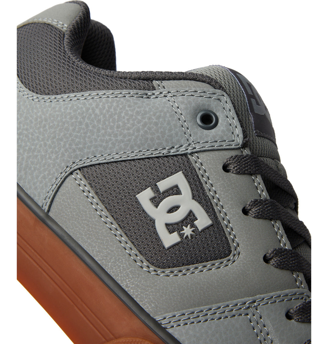 Close-up of a gray sneaker with black laces, textured detailing, and a brown sole. The DC Shoes Men’s Pure Shoes feature a bold white DC logo on the side panel, offering both comfort and versatile style for everyday wear.