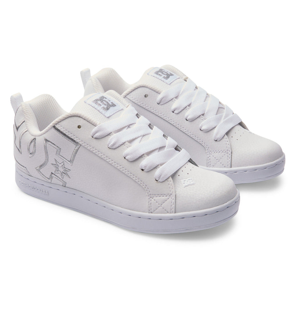 A pair of Women’s Court Graffik Shoes by DC Shoes, featuring a white chunky silhouette with thick white laces and a silver DC logo on the side, displayed on a white background and evoking classic ‘90s style.