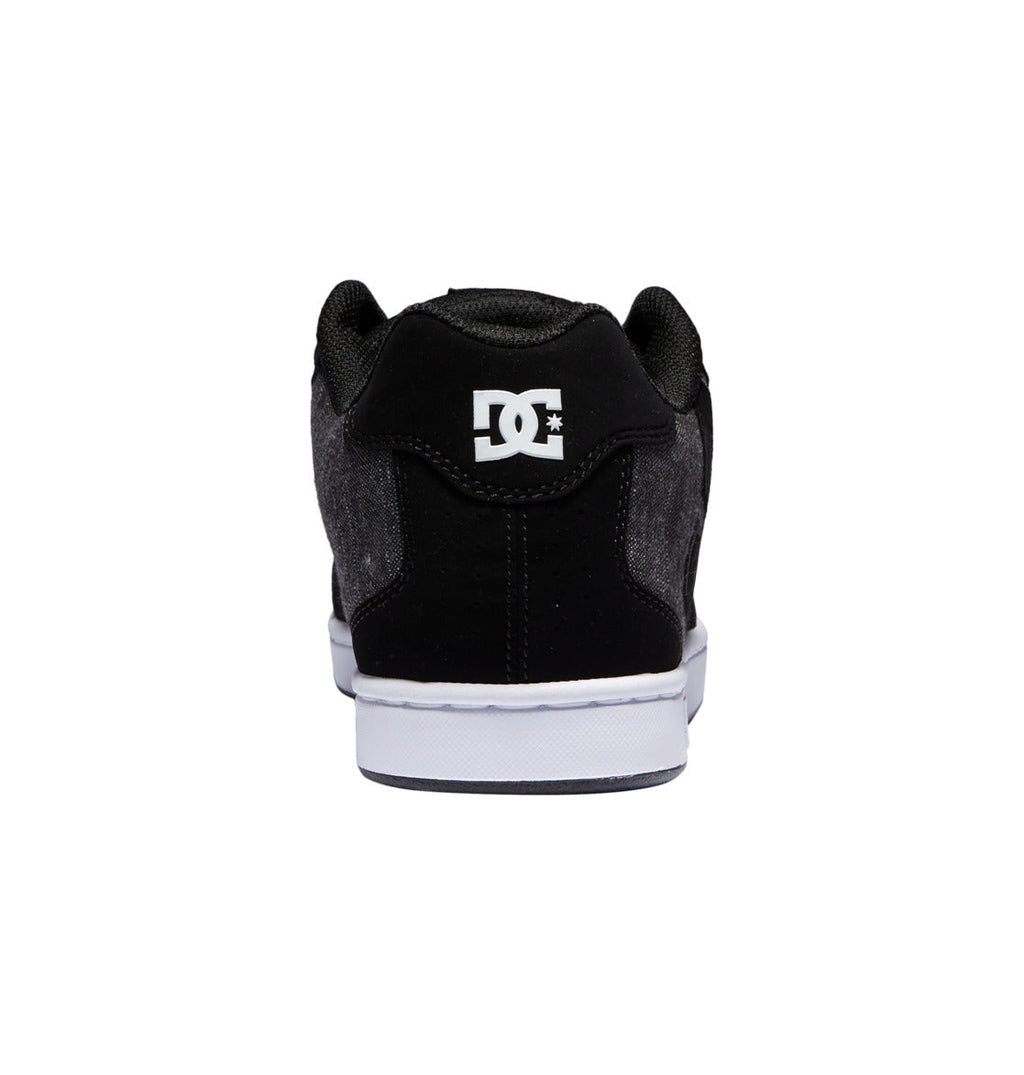 A rear view of the DC Shoes Men’s Net Shoes in black is displayed, featuring a white sole and the DC Shoes logo in white on the heel, set against a plain white background.
