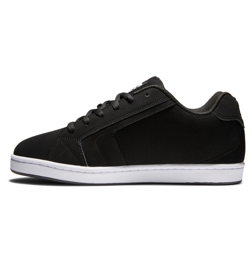 The DC Shoes Men’s Net Shoes are black low-top sneakers crafted from durable fabrics, featuring black laces, black stitching, a white rubber sole, and bold DC branding in the signature puffy sneaker style. Shown in a side profile on a plain white background.