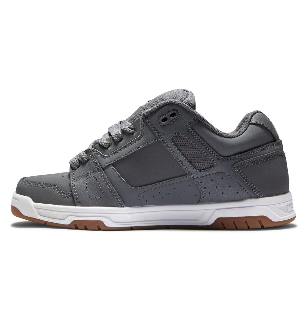 A side view of the DC Shoes Men’s Stag Shoe in gray, featuring a durable white and brown rubber cupsole, an oversized puff padded collar, and gray laces, displayed against a white background.