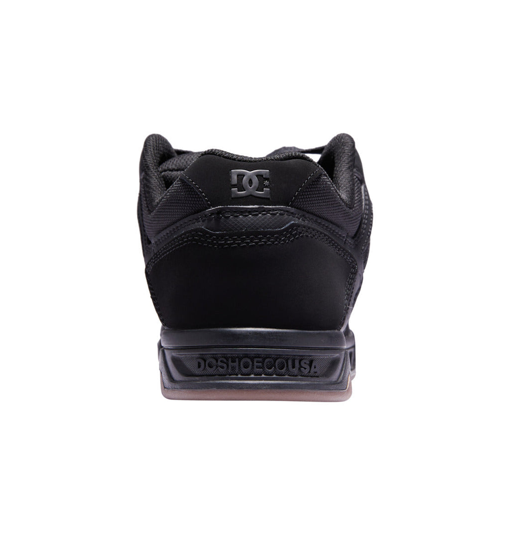 Back view of the DC Shoes Men’s Stag in black, with ‘DCSHOECOUSA’ embossed on the heel and the DC logo on the tongue, featuring an oversized puff and durable cupsole construction, shown against a white background.