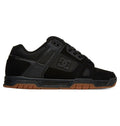 The DC Shoes Men’s Stag Shoes are shown in side view against a white background, featuring a black low-profile design with mesh and suede uppers, black laces, perforated panels, and a durable brown cupsole.
