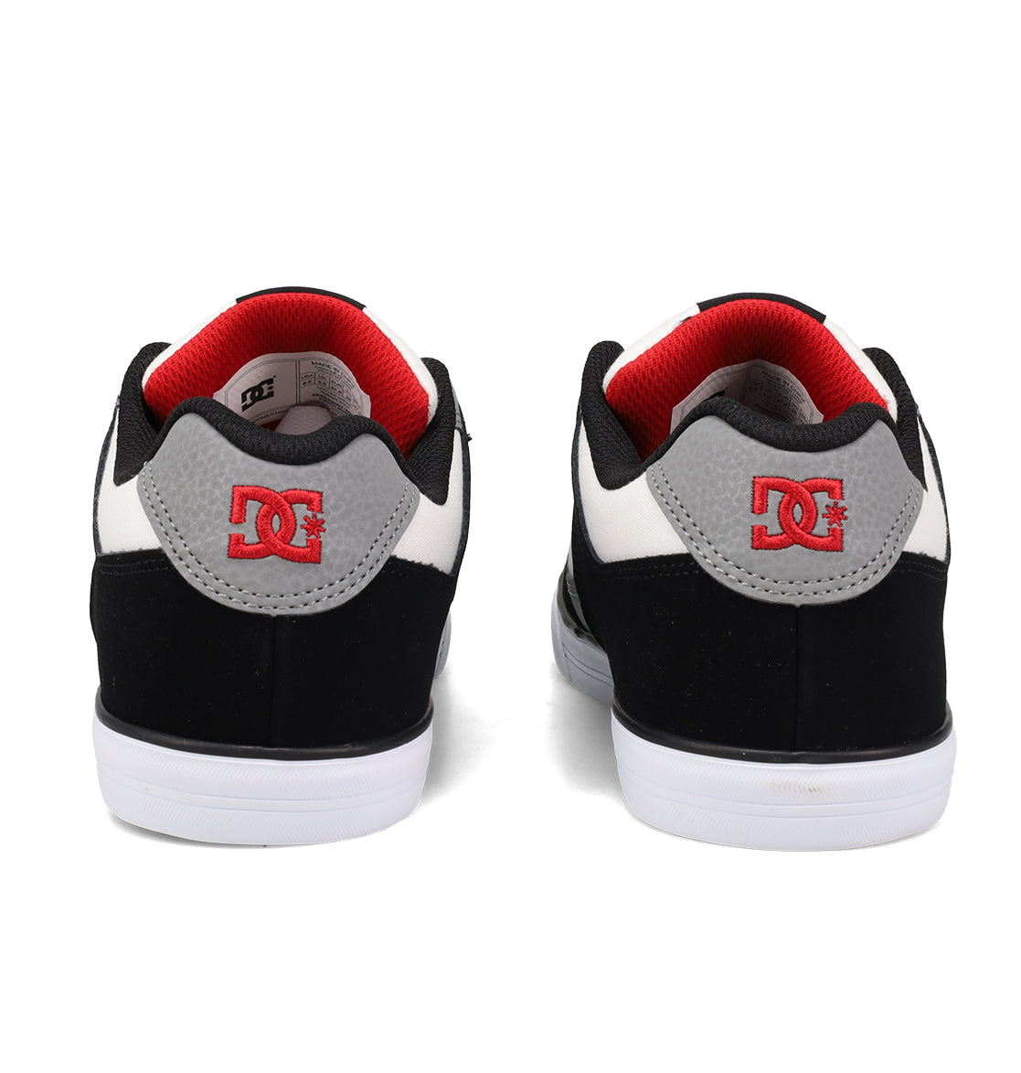 A pair of DC Shoes Kids’ Pure Shoes in black, white, and gray seen from the back, featuring red DC logos on the heels and red lining inside. Designed for both comfort and durability, these shoes are ideal for active young skaters.