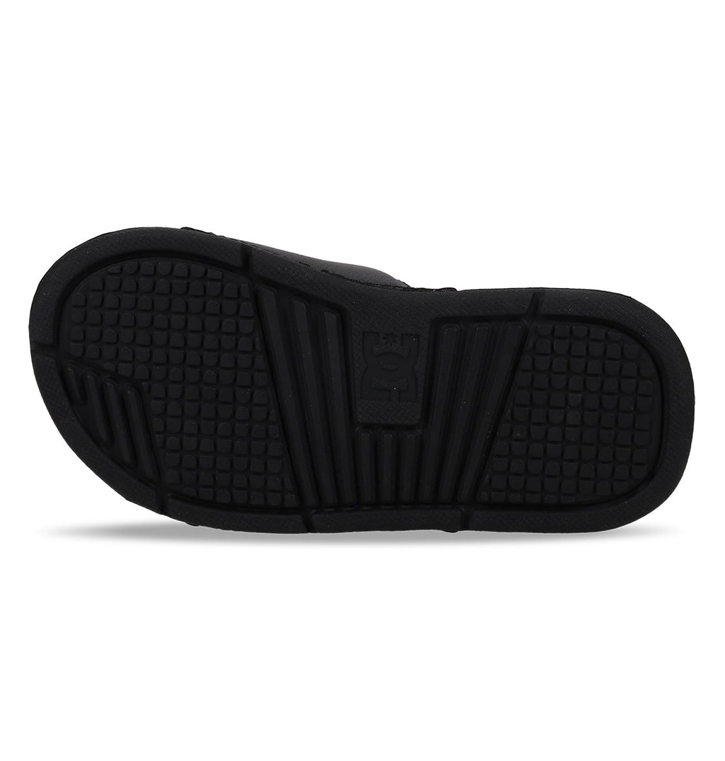 The image shows the black rubber sole of DC Shoes Kids' Bolsa Slides, featuring square-patterned treads and grooves for grip, plus a raised logo in the center—ideal for comfy kids slide sandals.