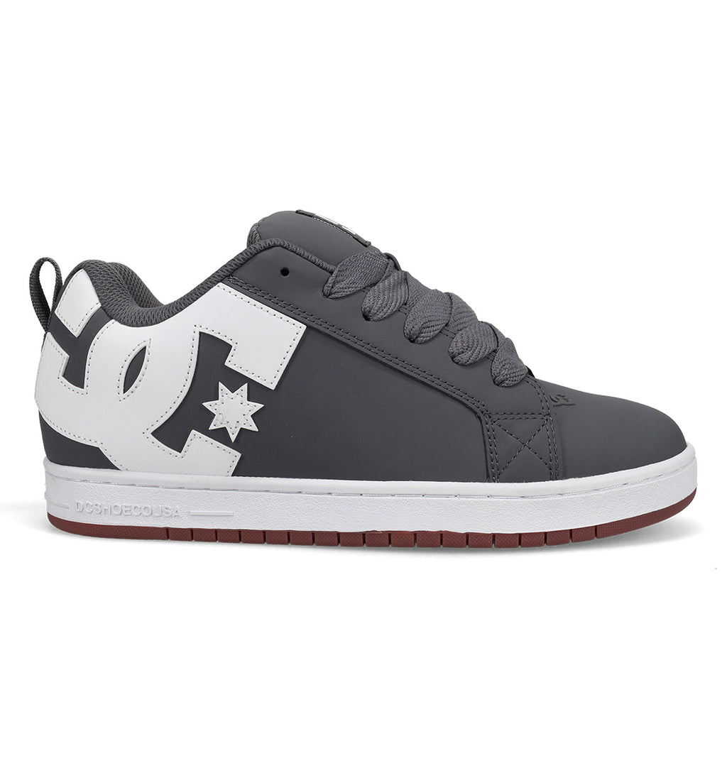 A gray and white men’s skate shoe from DC Shoes’ Court Graffik line, featuring a prominent white DC logo on the side, gray laces, and a white sole with a red-brown bottom.