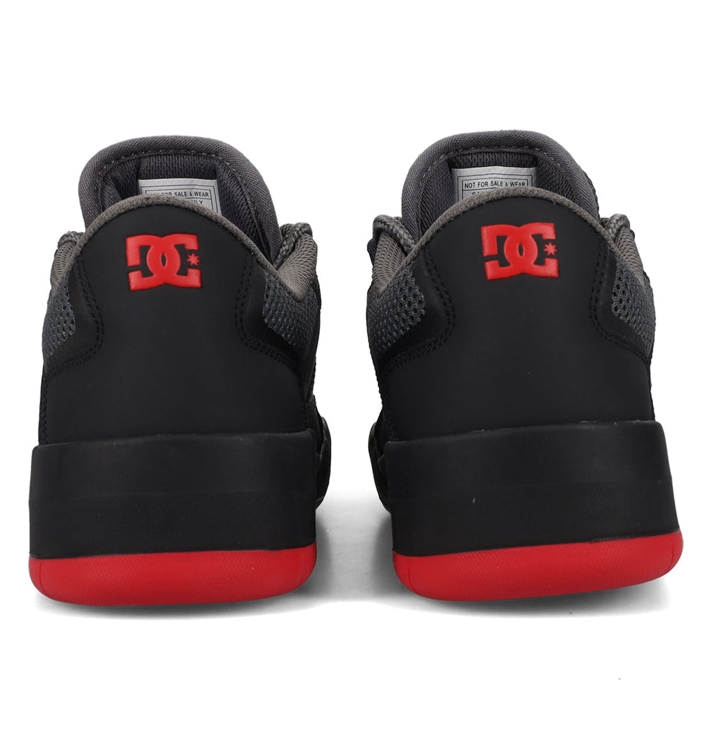 A pair of DC Shoes Men’s Metric Shoes in black with gray accents and vibrant red soles, shown from the back. The heels showcase a bold red DC Shoes logo, making these black, gray, and red sneakers a standout addition to any collection.