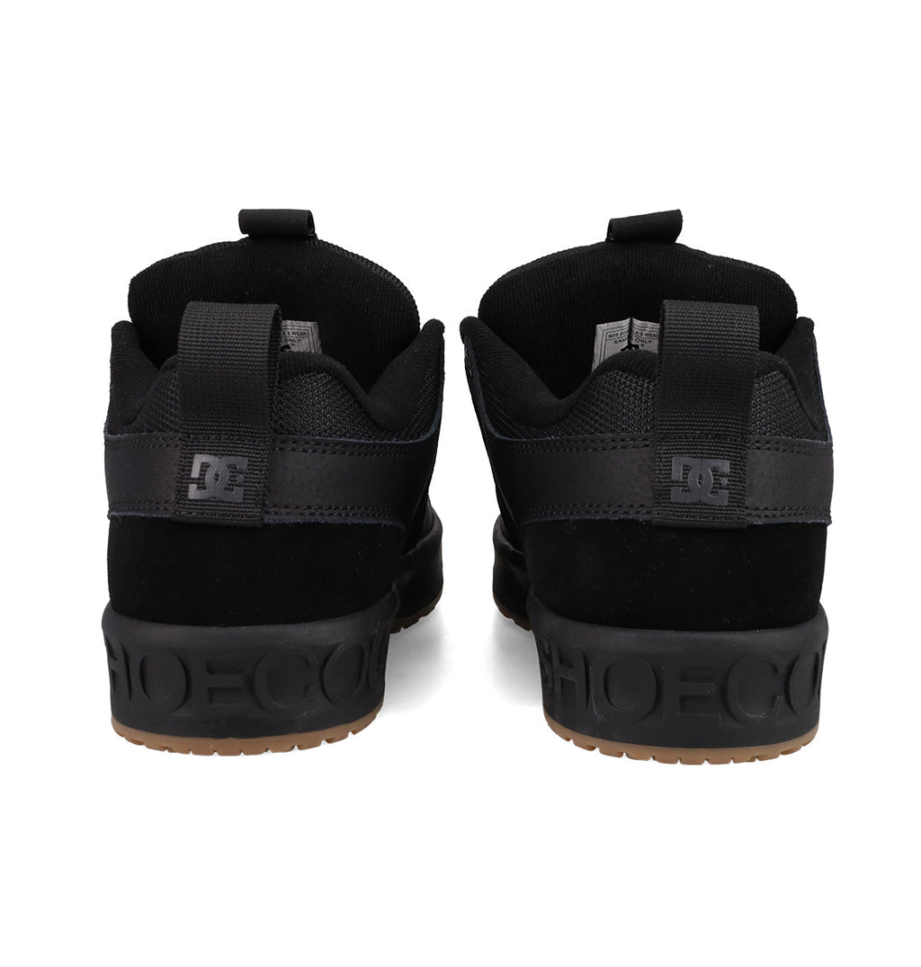 A pair of Men's Lynx OG Shoes by DC Shoes, in black, viewed from the back with DC logos on the heels, SHOECOUSA embossed on black midsoles, and gum rubber outsoles—an iconic skateboarding favorite.
