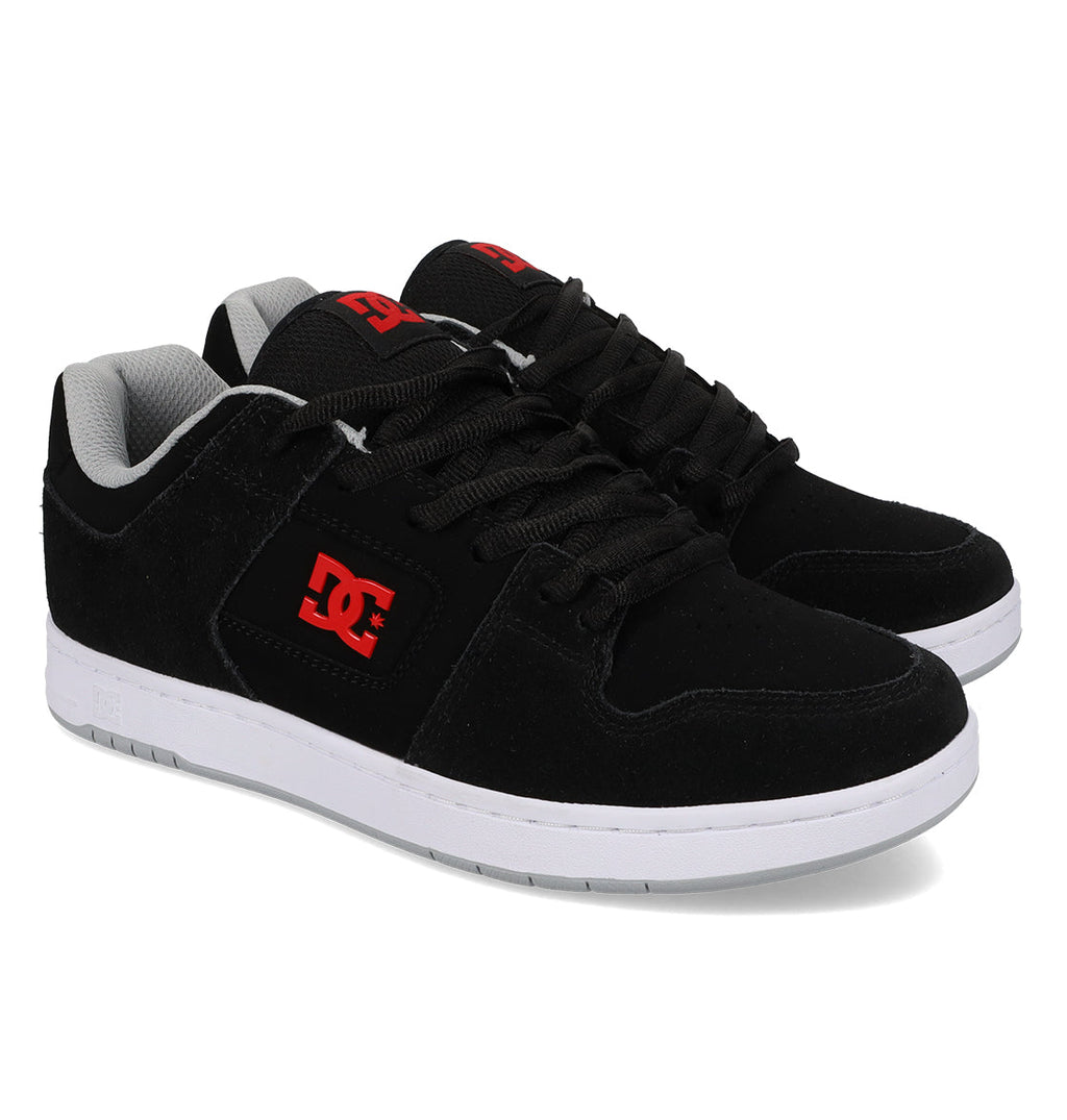 A pair of Men’s Manteca 4 Shoes by DC Shoes in black, featuring white soles and red DC logos on the side and tongue, designed for modern comfort and displayed at an angle on a white background.