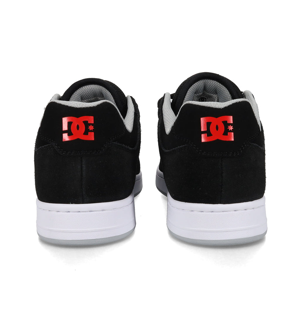 Rear view of a pair of black DC Shoes Men’s Manteca 4, featuring white soles and red DC logos on the heels, positioned side by side against a white background. Engineered for modern comfort, these skate shoes deliver both style and support for every session.