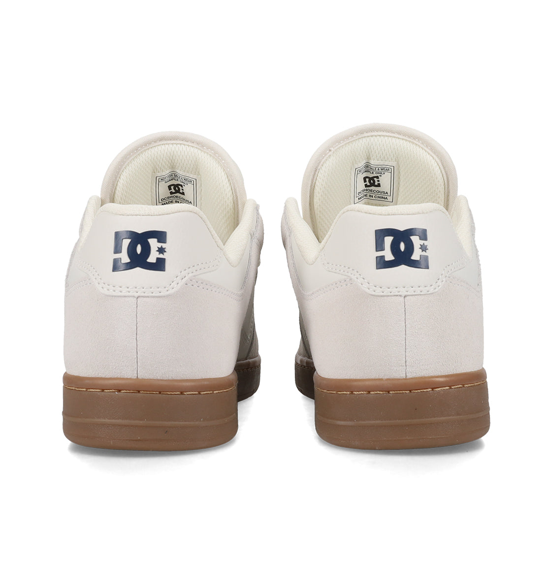 Two white Men’s Manteca 4 Shoes from DC Shoes, featuring tan soles, are displayed from the back. The performance-focused design highlights the iconic DC Shoes logo in dark blue on each heel, with insides and tags also partially visible.