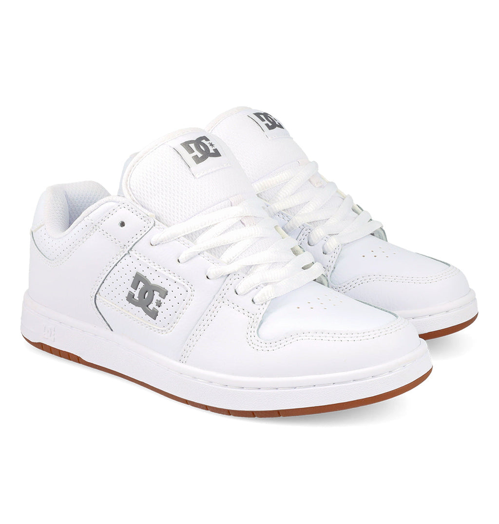 A pair of DC Shoes Women’s Manteca 4 Shoes, featuring a white colorway with white laces, grey DC logos on the side and tongue, and brown rubber soles—highlighting their performance-focused design—are displayed against a white background.