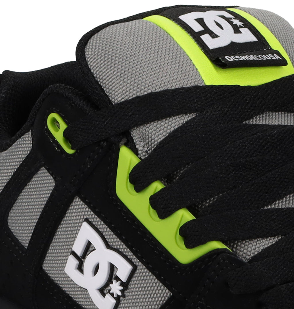 Close-up of DC Shoes Men's Stag Shoes featuring a gray mesh dynamic upper, black accents, neon yellow eyelets, and white DC Shoes logos on the side and tongue. Durable cupsole ensures lasting support.