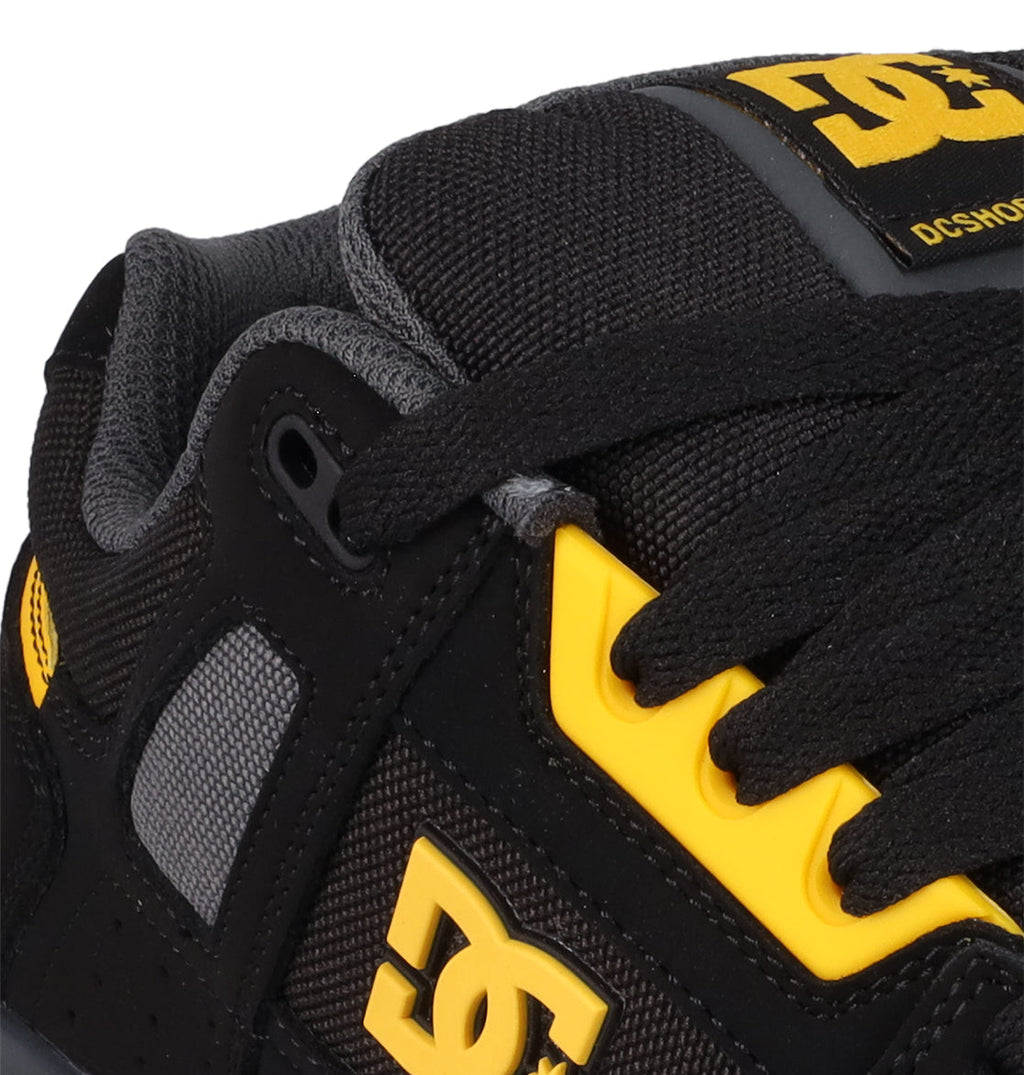 Close-up of the Men's Stag Shoes by DC Shoes in black with yellow accents, gray mesh details, black laces, and a padded tongue with a yellow logo. Features a durable cupsole inspired by skate culture.