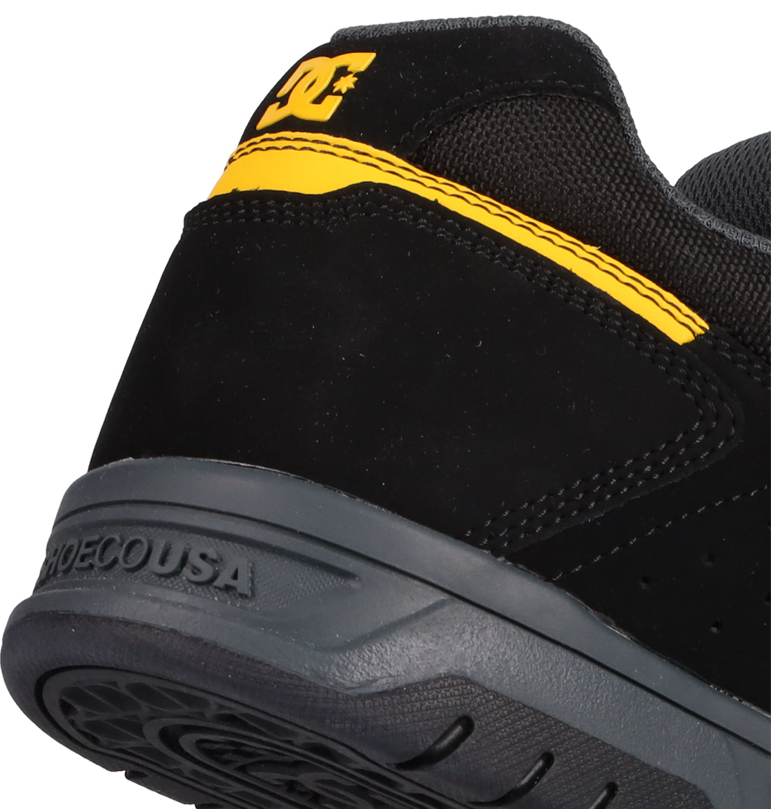 Close-up of the heel of the Men's Stag Shoes by DC Shoes. This black shoe features a yellow accent, DC logo on the back, and a durable dark gray cupsole embossed with SHOESCOUSA, capturing classic skateboarding style.