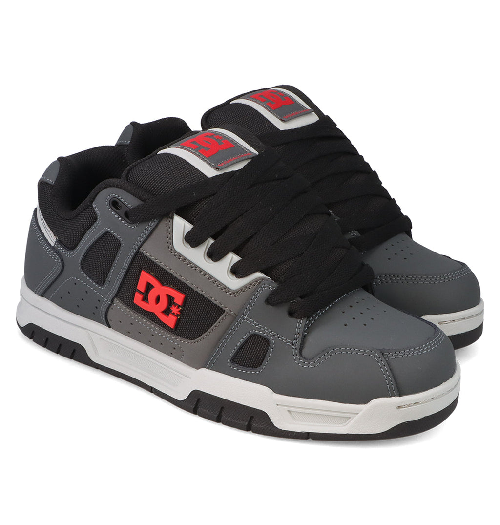 A pair of DC Shoes Men’s Stag Shoes in gray, featuring black laces, black soles with white midsoles, and bold red DC logos on the tongue and side—ideal for anyone who loves classic skate culture style.