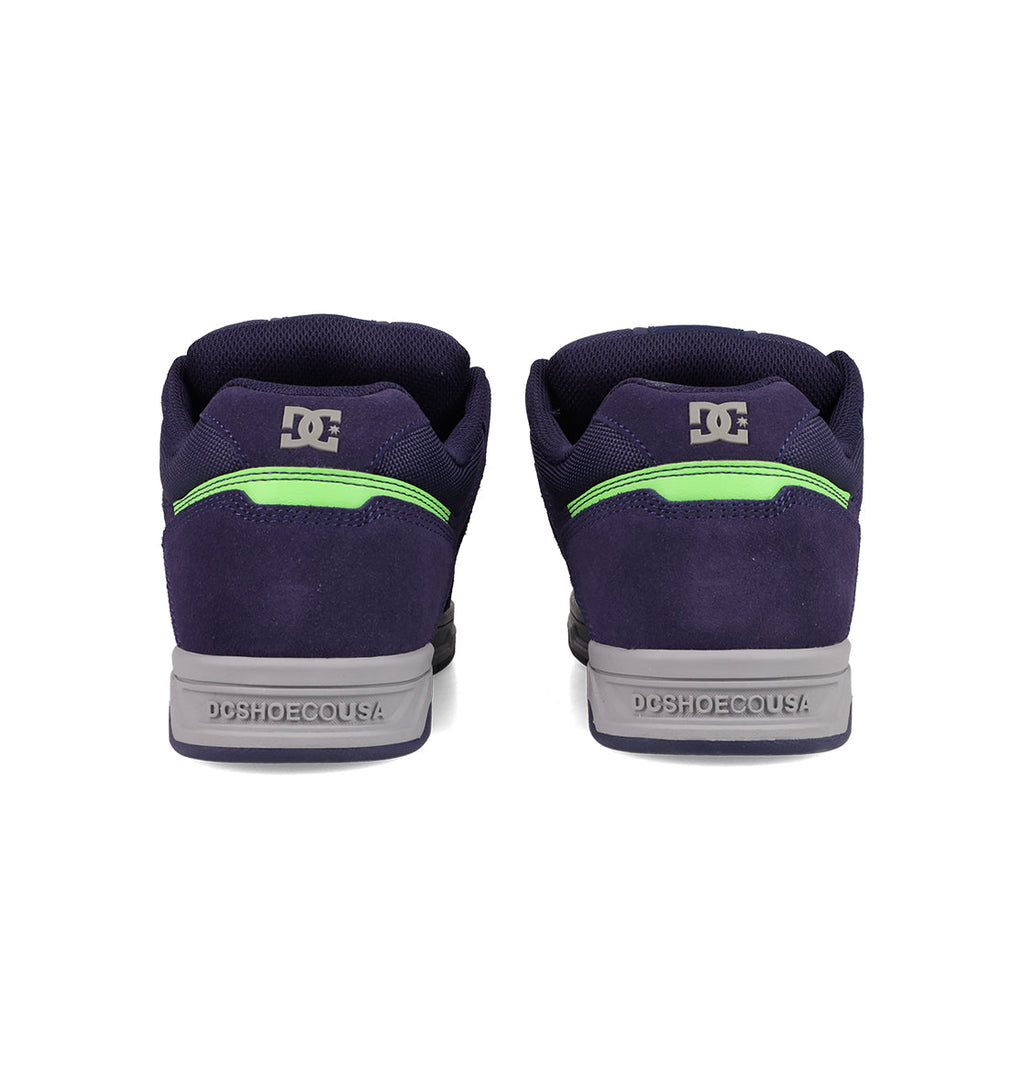 Men's Stag Shoes by DC Shoes in navy blue, shown from the back, have gray cupsoles, neon green details, and DC logos on heel and collar—ideal for skate culture fans.