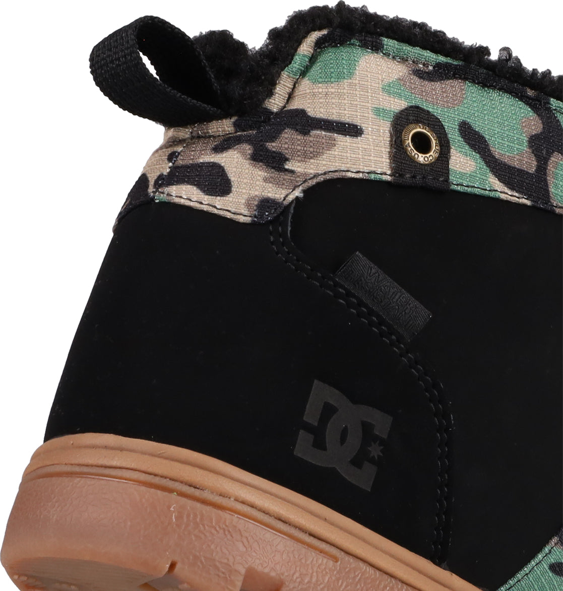 Close-up of the heel of the Men's Woodland Winter Boots by DC Shoes, featuring a black suede lower, brown rubber sole, green and beige camouflage upper, and the DC Shoes logo—combining rugged boot vibes with modern style.