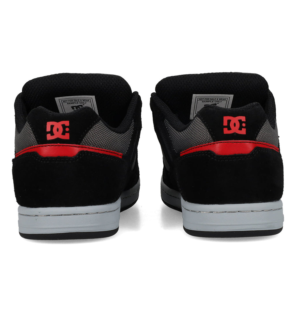 A pair of Kids’ Stag Shoes by DC Shoes, shown from the back, featuring red DC logos on the heels and gray rubber soles for enhanced impact absorption.