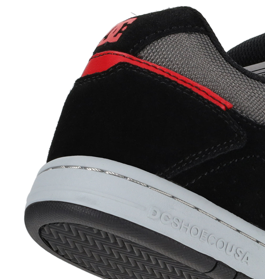 Close-up of the heel of the DC Shoes Kids’ Stag sneaker in black and gray with red accents and DCSHOECOUSA embossed on the white sole. The shoe features suede and mesh materials, offering lightweight cushioning for enhanced comfort and impact absorption.