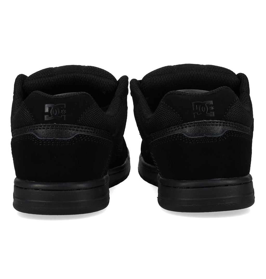 A pair of Kids’ Stag Shoes by DC Shoes in black, viewed from behind to highlight the heel, durable cupsole, and the logo on the back of each shoe against a white background.