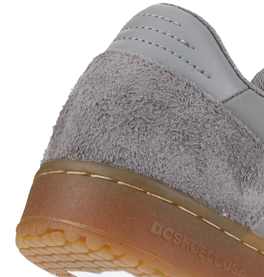 Close-up of the heel of a Men’s Astrix Shoe by DC Shoes in gray, showcasing its suede texture and brown rubber sole with visible stitching details and part of the textured tread underneath—designed for street skateboarding to provide enhanced board control.