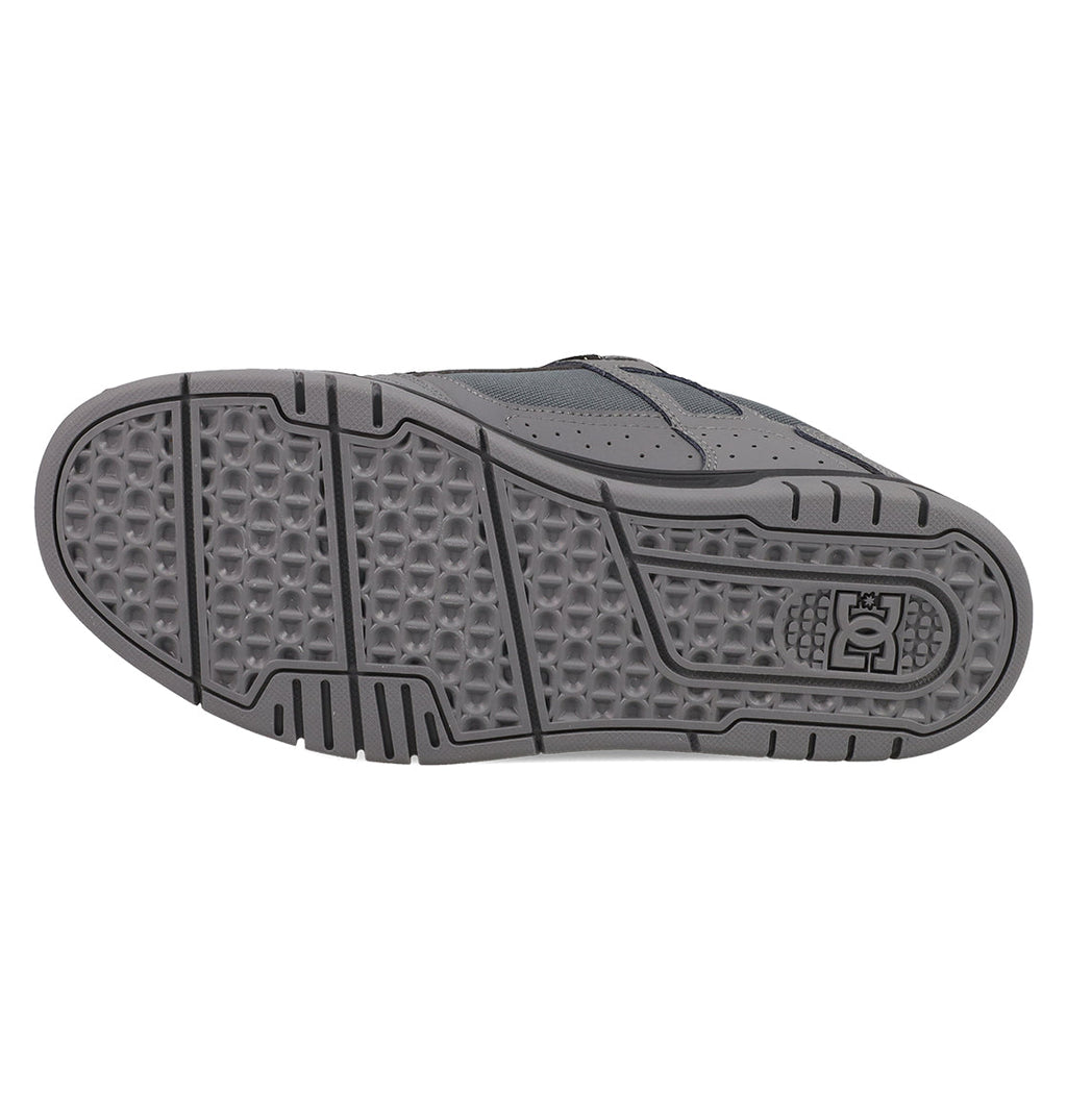 The image shows the gray rubber sole of DC Shoes Men's Stag Shoes, featuring geometric tread patterns for grip, a durable cupsole design, and the DC logo by the heel—ideal for skate culture fans.