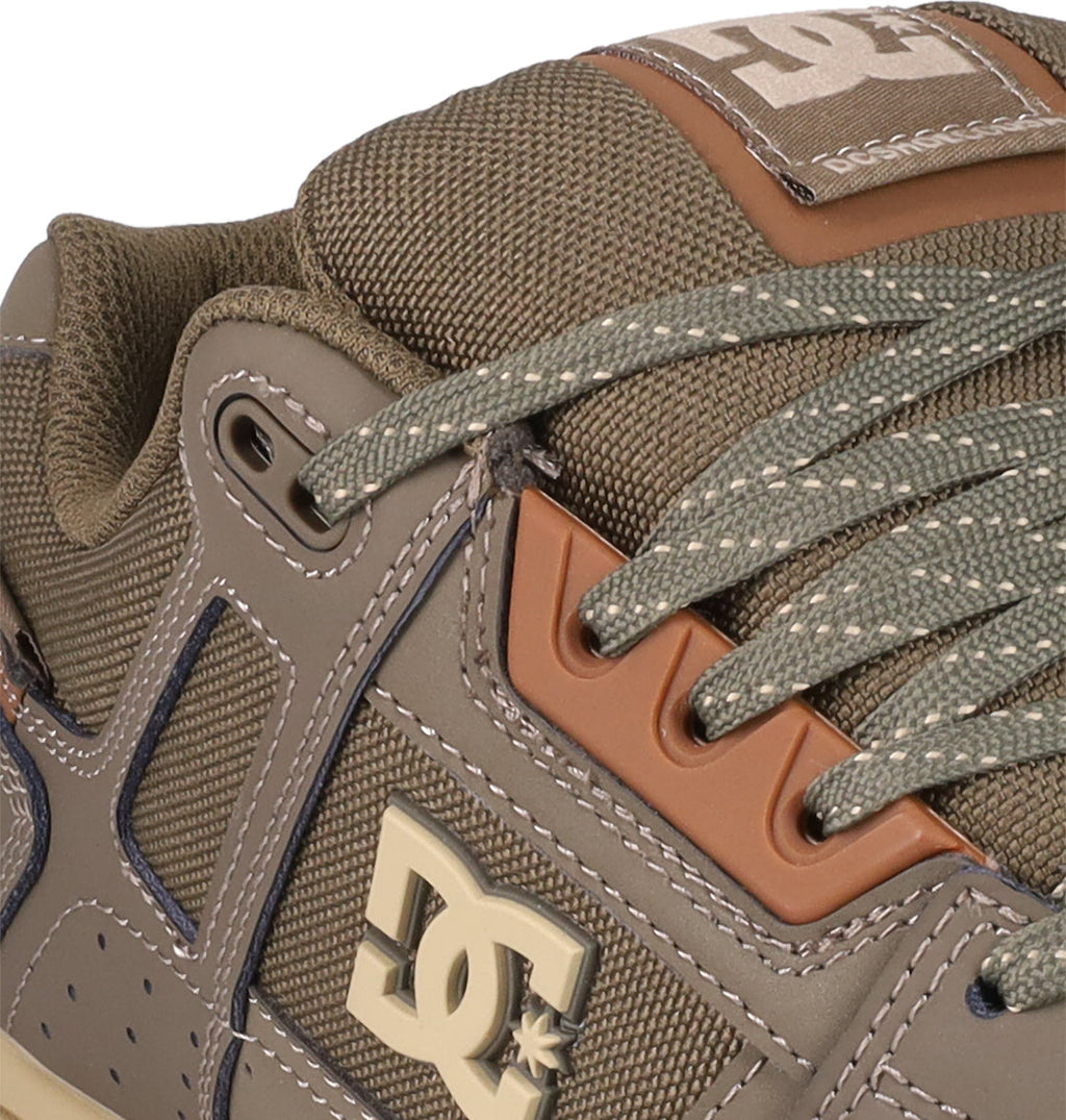 Close-up of DC Shoes Men's Stag, showcasing olive green and brown tones, textured fabric tongue, detailed stitching, brown eyelets, and green laces. Features a bold DC logo and durable cupsole for classic skate-inspired style.