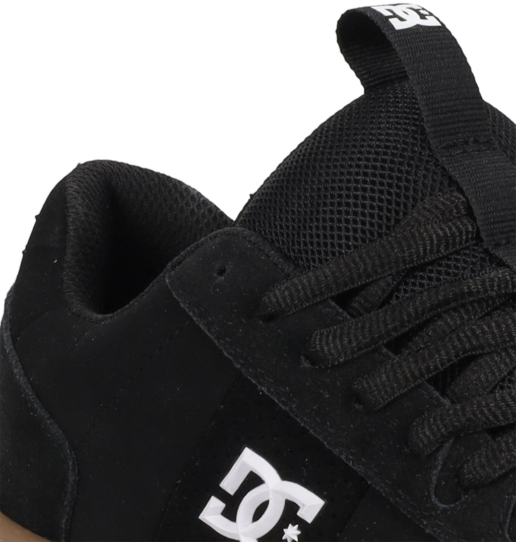 Close-up of a black DC Shoes Men’s Astrix Shoe showing the side logo, black laces, mesh tongue, and a pull tab with the DC logo. Designed for street skateboarding, this shoe emphasizes board control. Only part of the shoe is visible against a white background.