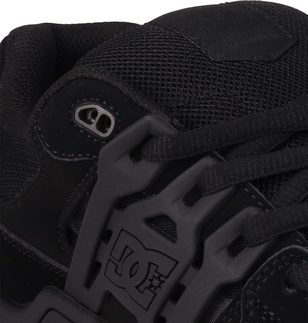 Close-up of DC Shoes Men's AT-2 skate shoe in black, featuring detailed stitching, black laces with metal eyelets, a DC Shoes logo on the plastic lace guard, and an Airband outsole.