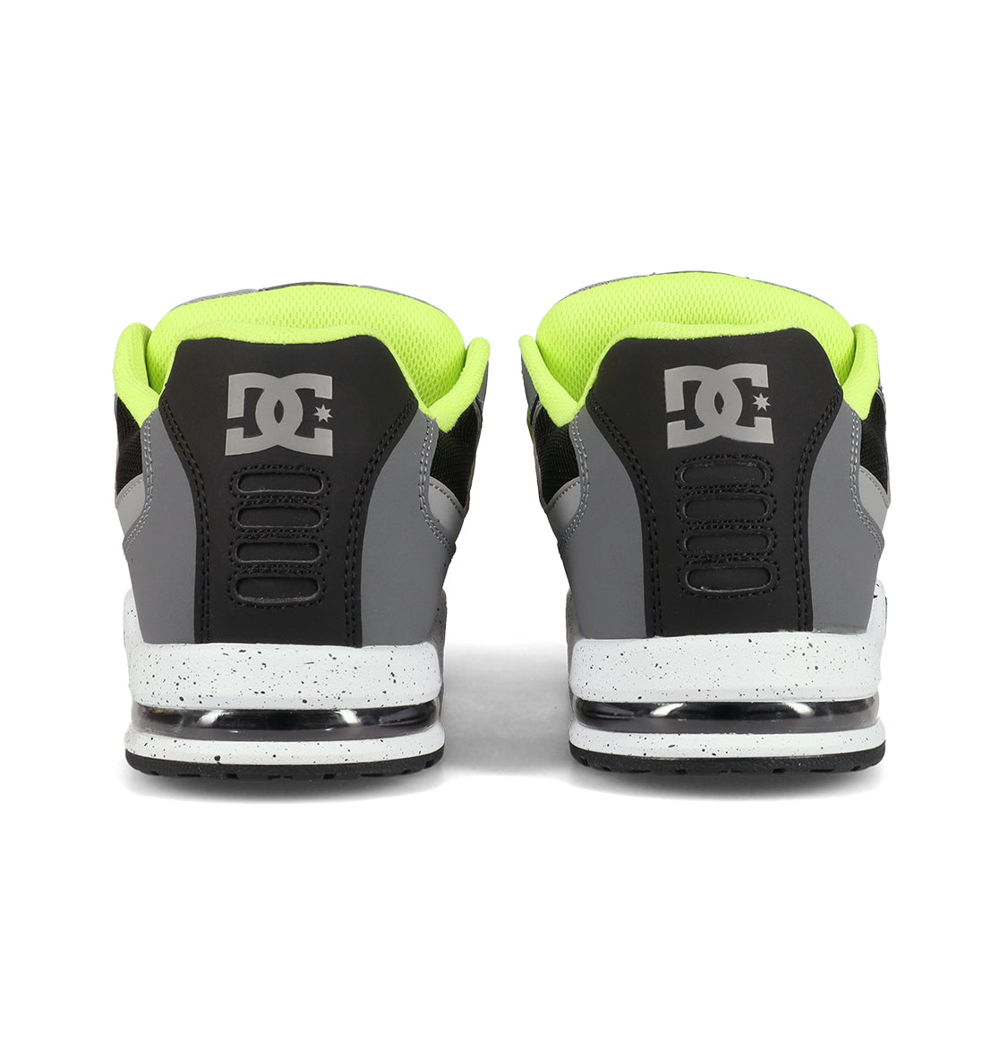 A pair of DC Shoes Men’s AT-2 Shoes is shown from the back, showcasing a black and gray color scheme accented by neon yellow lining and white speckled soles. The DC logo appears on each heel, while superior cushioning delivers lasting comfort with every step.