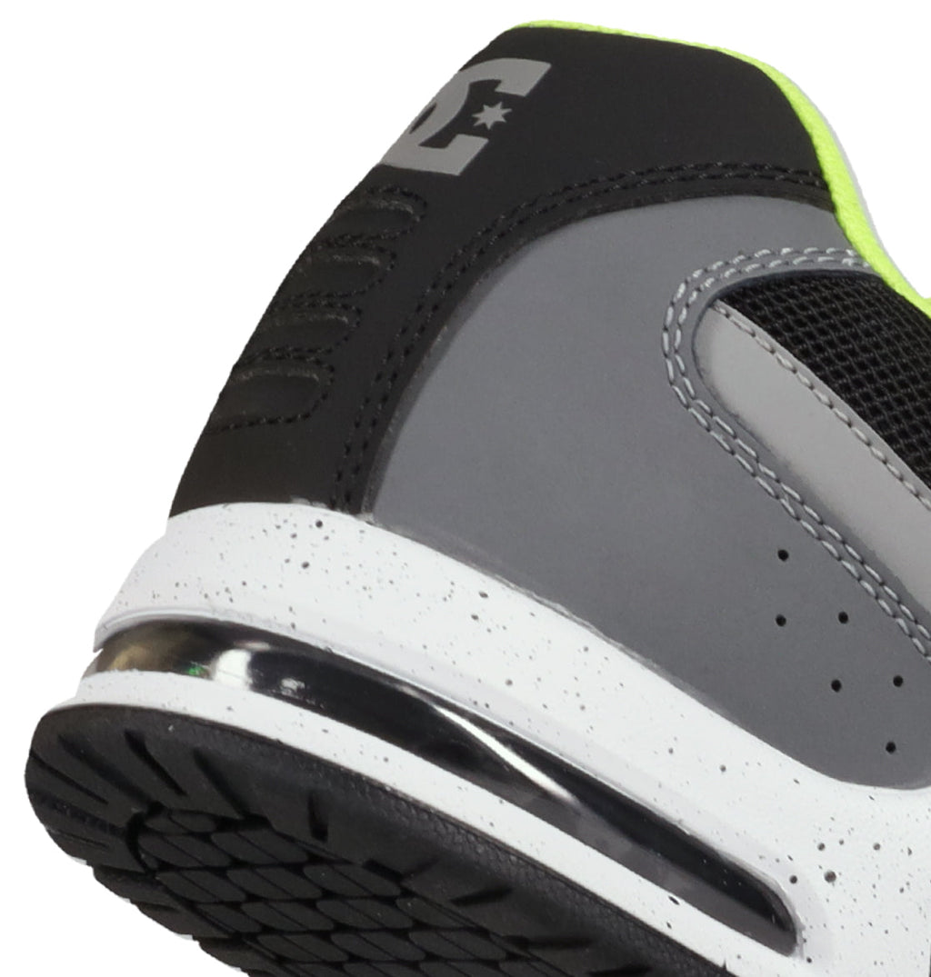 Close-up of the heel and side of the DC Shoes Men’s AT-2 Shoes in gray and black, featuring a white speckled midsole, visible tread pattern, and neon yellow lining. A supportive TPU cage enhances stability around the heel, while part of the DC “E” logo appears on the back.