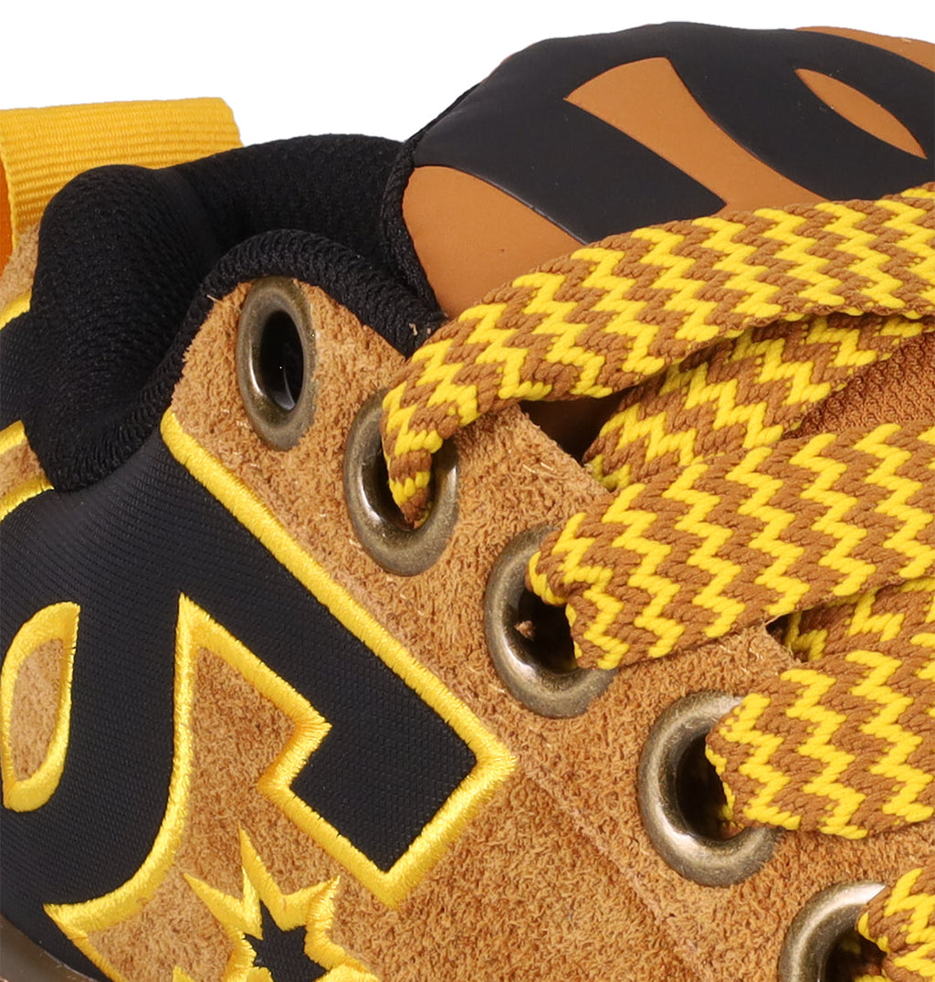 Close-up of DC Shoes Men's Court Graffik Puff Shoes in brown suede, featuring yellow and brown patterned laces, gold eyelets, black and yellow embroidered side details, and an exaggerated upper for a bold, modern look.