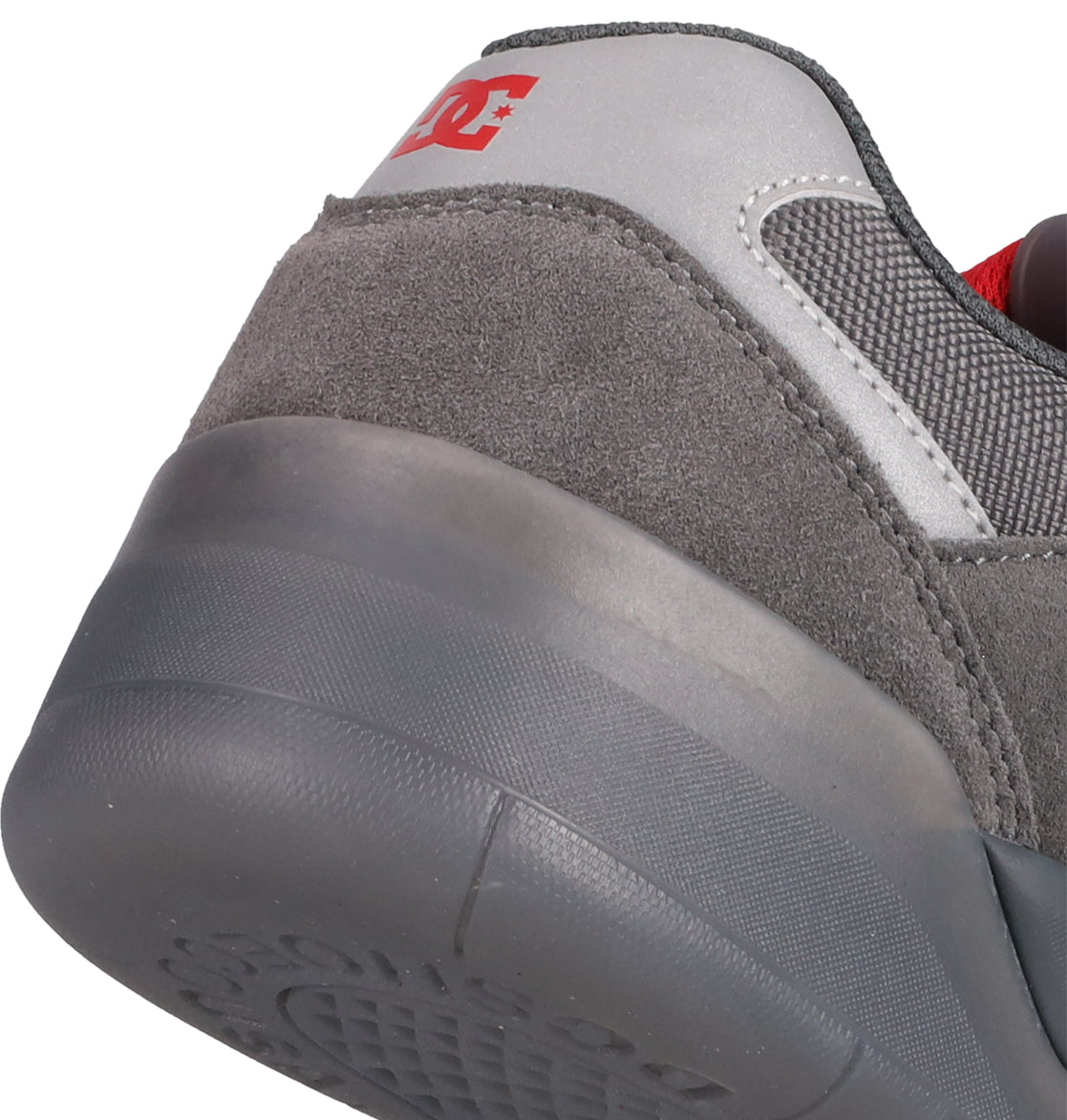 Close-up of the heel of a gray DC Shoes Men's Fractal SE skate shoe, featuring suede and mesh textures, a red DC logo on the silver collar, and a gray rubber sole for enhanced comfort and performance.