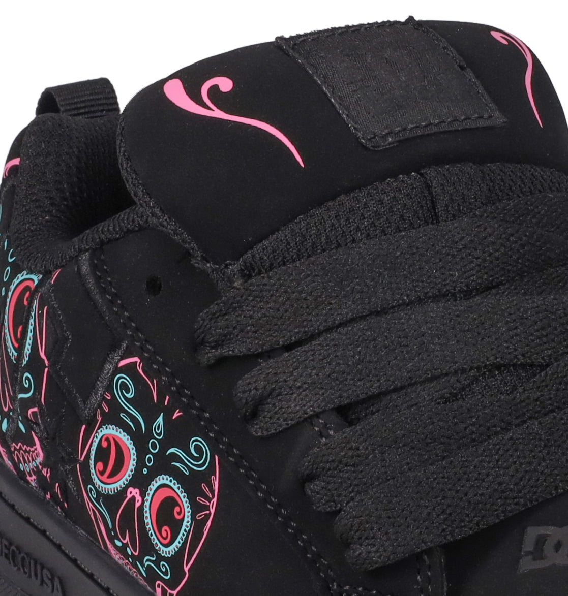 Close-up of the Kids’ Court Graffik Day Of The Dead sneaker by DC Shoes, showcasing thick black laces and vibrant pink and teal skull designs inspired by Día de los Muertos on the side and near the tongue. The black sneaker features a fabric pull tab and a plain black patch on the tongue.