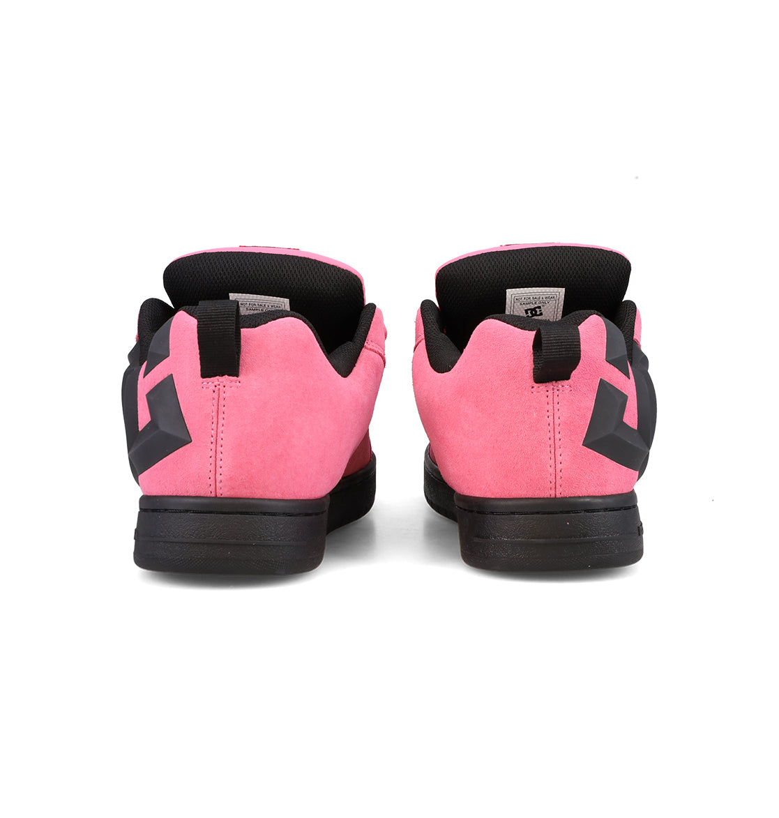 A pair of DC Shoes Men’s Court Graffik Beveled Special Edition sneakers in pink, featuring black soles and a black interior, is shown from the back. The heel areas display distinctive black geometric designs that highlight the iconic DC branding.