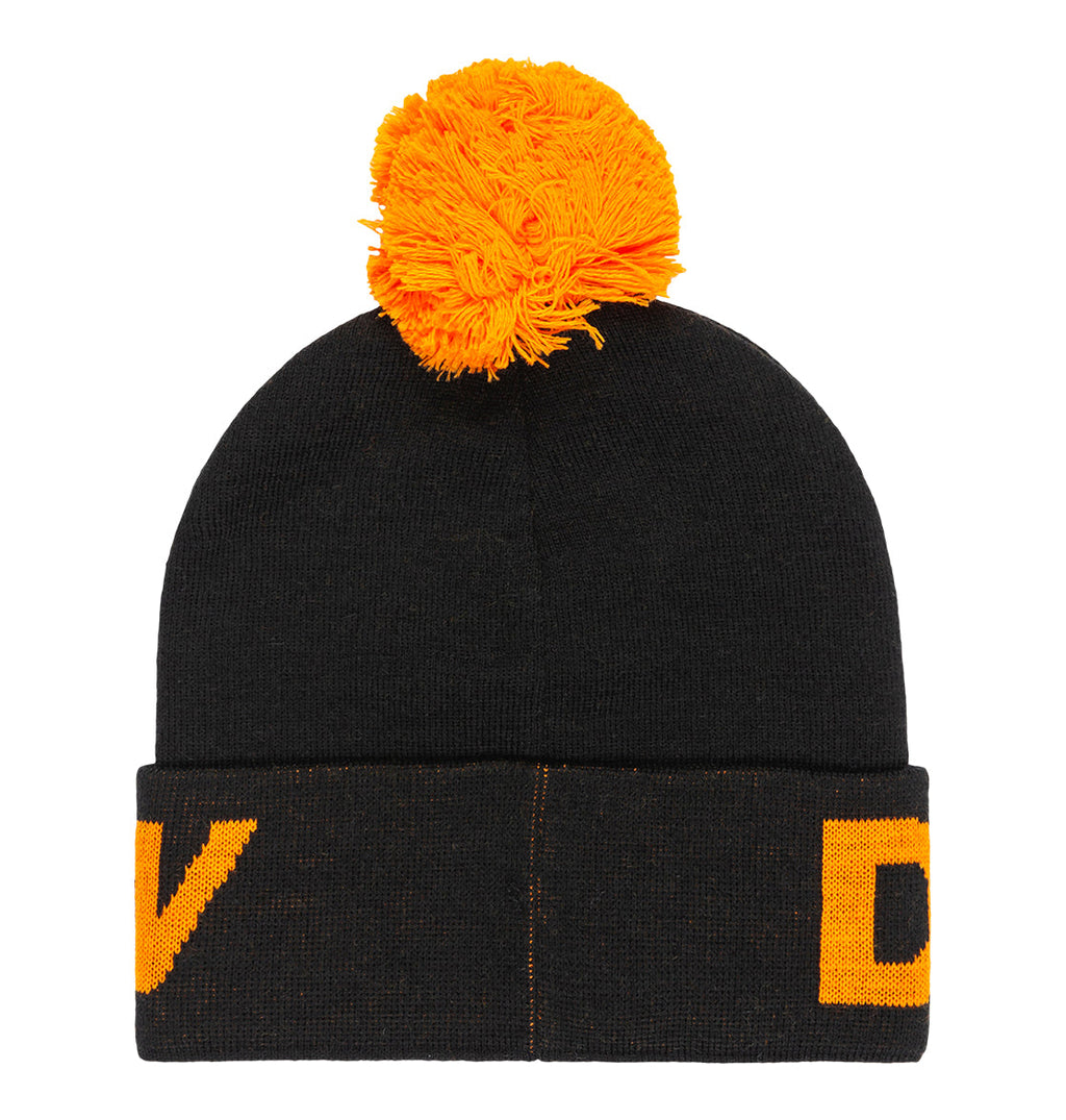 Introducing the Kids’ Gambol Beanie by DC Shoes—a stylish black knit winter hat made from recycled polyester, featuring a large, bright orange pom-pom on top and bold orange DC Shoes branding partially visible on the fold—perfect for kids looking for a warm and trendy beanie.