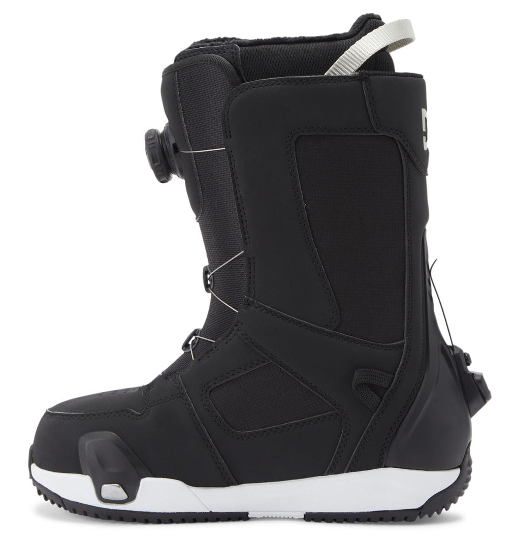 The DC Shoes Women’s Phase Pro Step On BOA® Snowboard Boots are shown in a profile view against a plain white background, featuring a black design with a white pull loop at the top, a side-mounted BOA® Fit System dial lacing system, and a thick, textured sole in white and black.