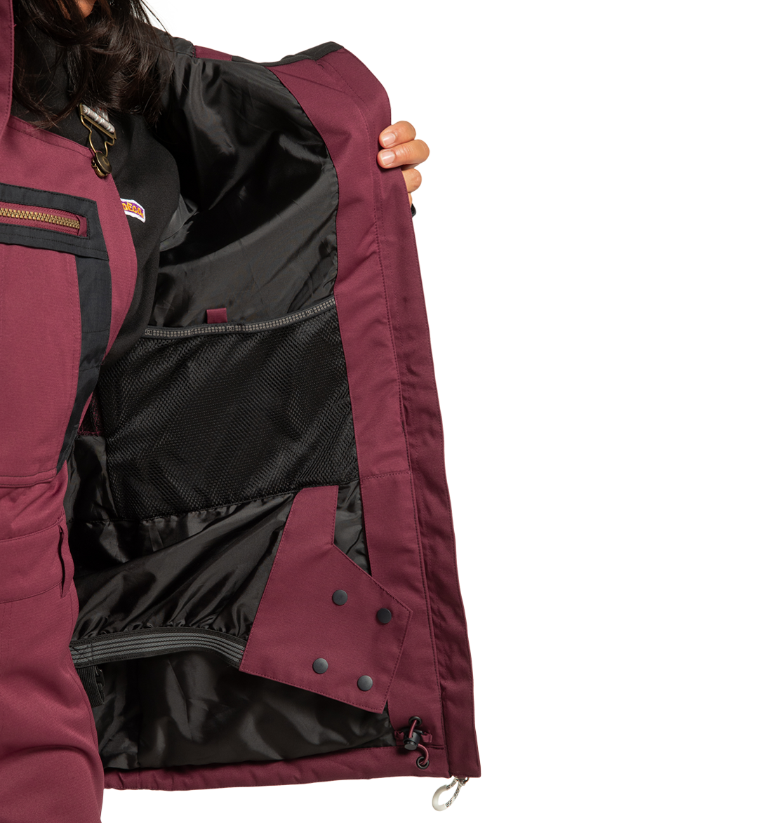 A person holds open the DC Shoes Women’s Liberate Insulated Jacket in maroon, revealing its black mesh inner pocket, cozy lining, and secure snap closures—ideal for winter adventures. Their face is hidden against a plain white background.