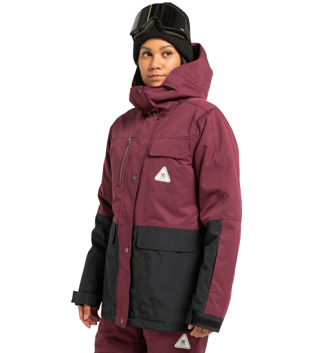 A person wearing a maroon and black DC Shoes Women’s Liberate Insulated Jacket, matching pants, a black beanie, and ski goggles stands against a plain white background—prepared for any winter adventure with reliable weather defense.