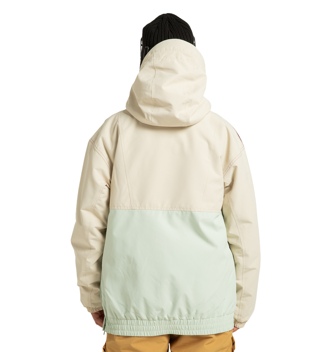 A person stands with their back to the camera against a plain white background, wearing the DC Shoes Women’s Chalet Anorak Insulated Jacket in a cream and light green color-blocked design, paired with brown pants and a black beanie.