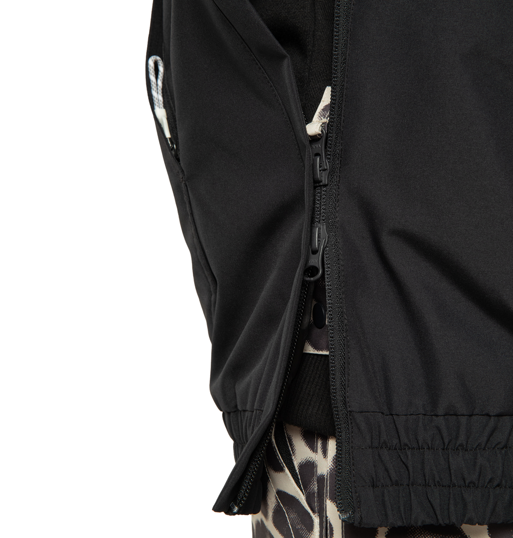 Close-up of the DC Shoes Women’s Chalet Anorak Insulated Jacket in black, with the zipper partially open to reveal a garment underneath featuring a black and beige giraffe print pattern.