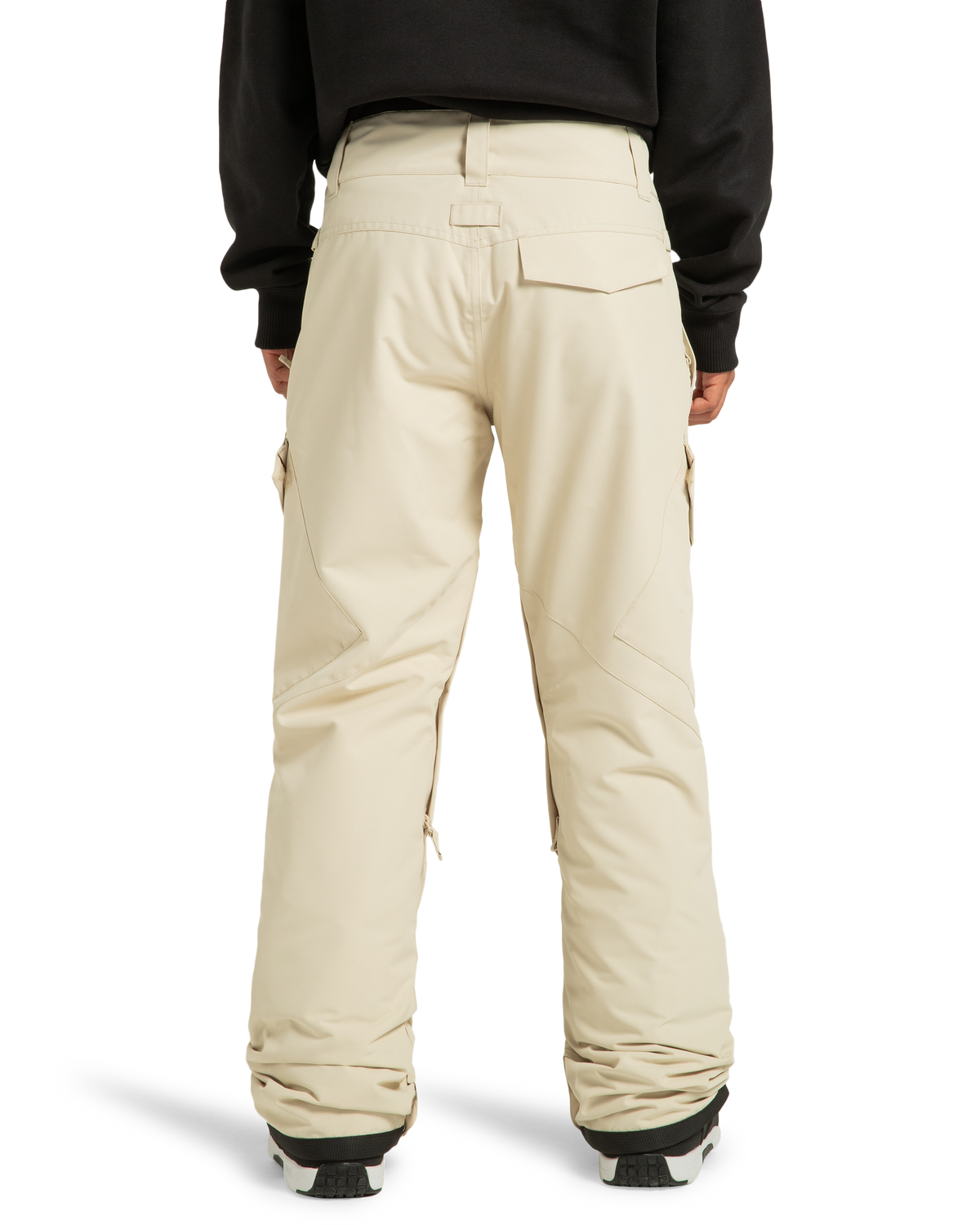 A person is shown from the back wearing DC Shoes Women’s Nonchalant Insulated Snow Pants in beige and a black jacket. The insulated snow pants feature pockets and seam details, with black and white boots partially visible at the bottom.
