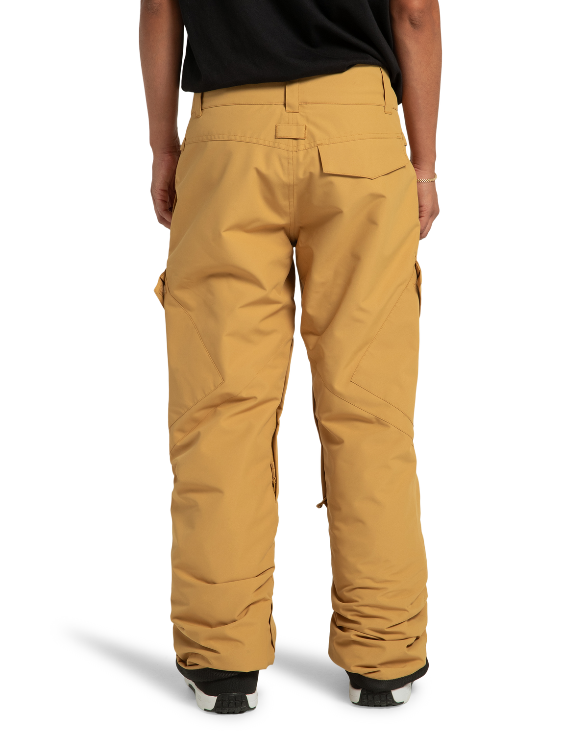 A person is seen from behind wearing DC Shoes Women’s Nonchalant Insulated Snow Pants in tan, paired with a black shirt. The sustainable snow pants, crafted from recycled polyester, feature side pockets and reinforced cuffs. Partially visible are white and black shoes.