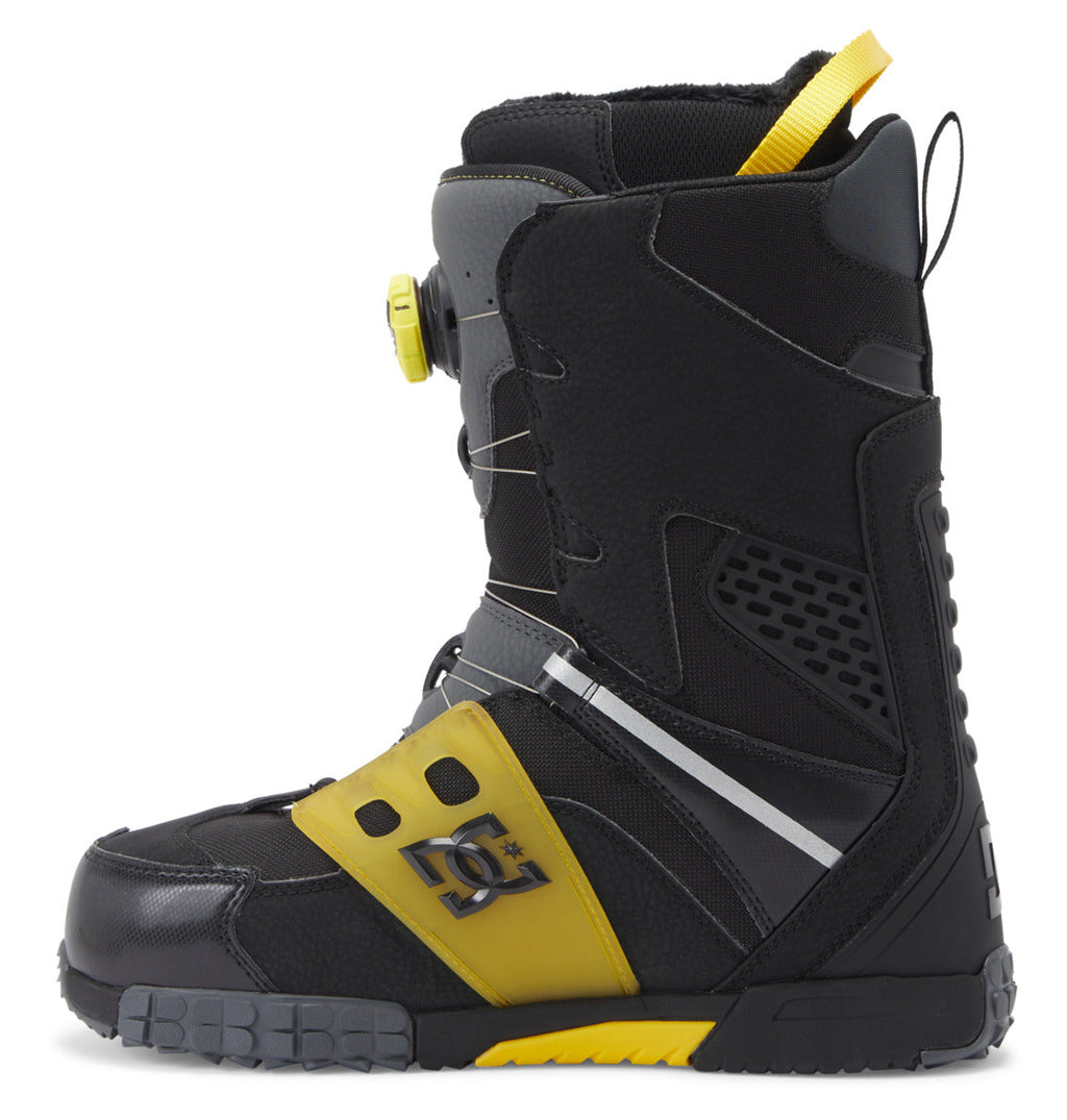 The DC Shoes Men’s Phantom BOA® Snowboard Boots are shown in a left side profile view, featuring a black design with yellow and gray accents, a yellow pull tab, a circular BOA® Fit System tightening mechanism, and a sturdy sole.