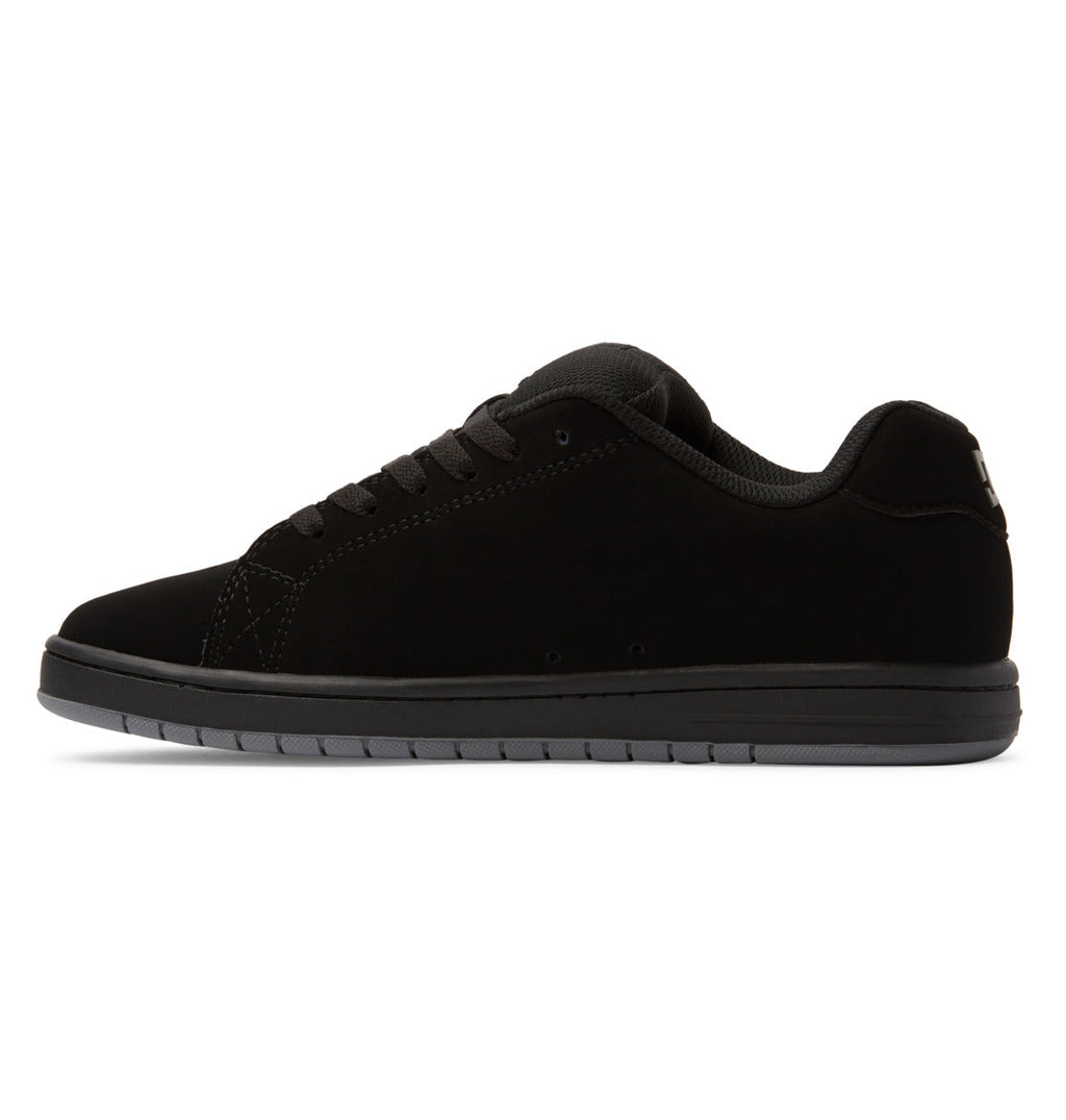 A side-profile view of the DC Shoes Men’s Gaveler Shoes is shown on a white background, highlighting their black low-top design with a suede-like texture, black laces, and a chunky dark gray rubber sole.