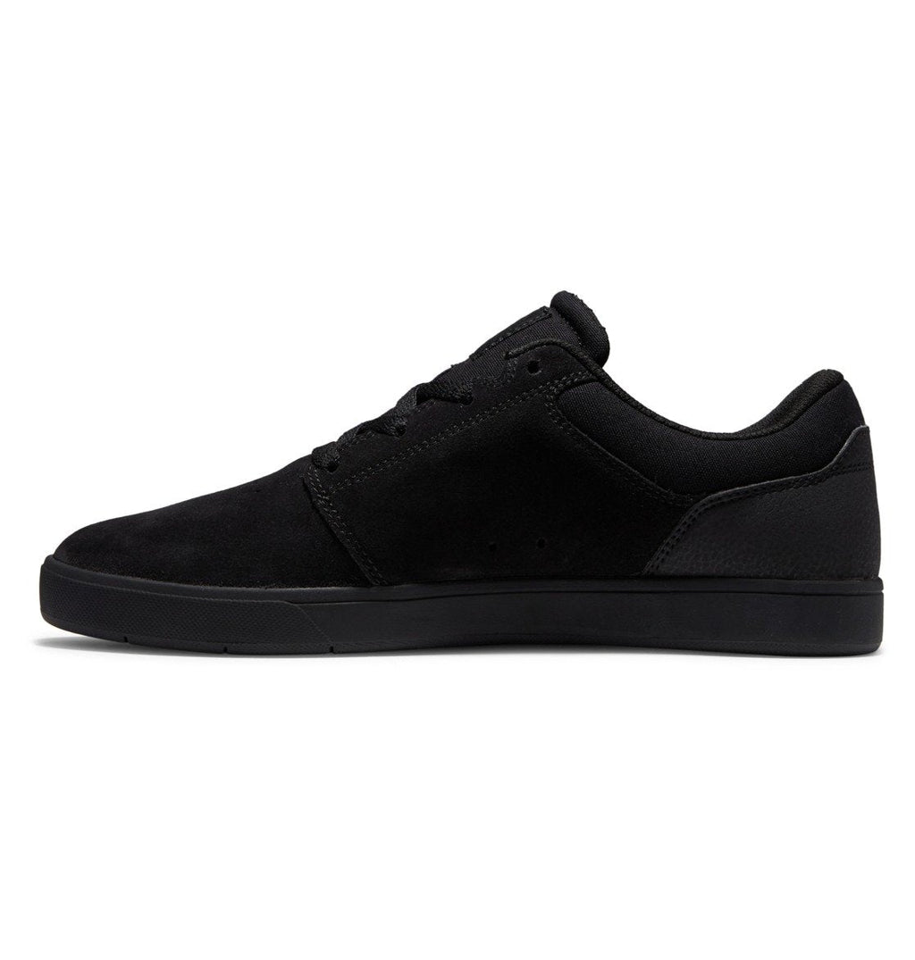 A side-profile view of the DC Shoes Men’s Crisis 2, a black low-top sneaker featuring a suede finish, black laces, and a performance cup sole, highlights how these skate shoes seamlessly combine style and function against a white background.