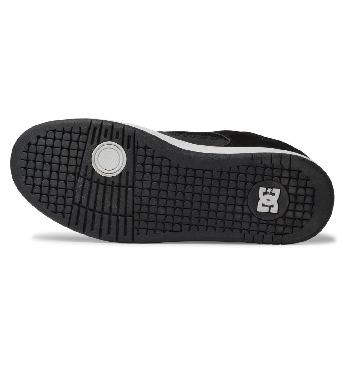 The image displays the black rubber sole of the Men’s Manteca 4 Shoes by DC Shoes, which features a circular tread pattern near the toe and a signature square logo with a crown and stylized E at the heel, emphasizing its performance-oriented design.